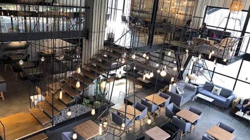 Two-floor open-plan interior of Almond Coffee House in Rabieh, Amman, with a mezzanine, staircase, hanging pendant lights and rows of wooden tables