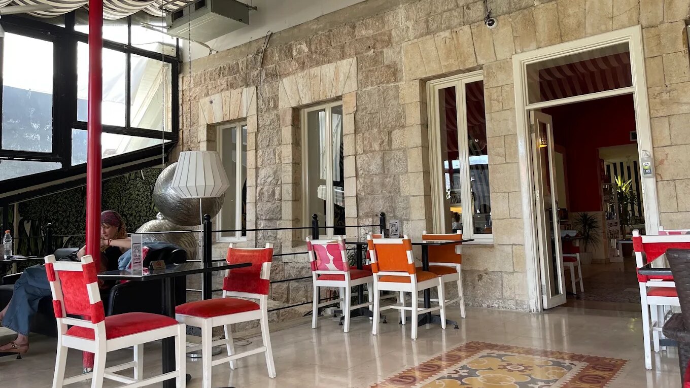 Covered terrace at Books@cafe in Jabal Amman, with limestone walls, a striped awning, red and orange chairs, patterned tiled floor and a customer working at a table