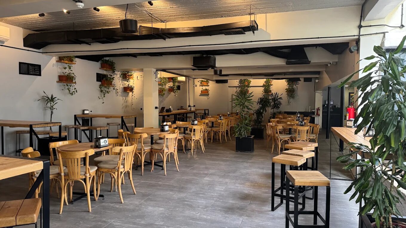 Large open room at Dali Space in Jabal Amman, with rows of wooden tables and bentwood chairs, high stools, hanging plants and an industrial ceiling