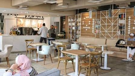 Bright spacious interior of Kitab Coffeehouse near University of Petra, Amman, with light wood tables, sofas and students working